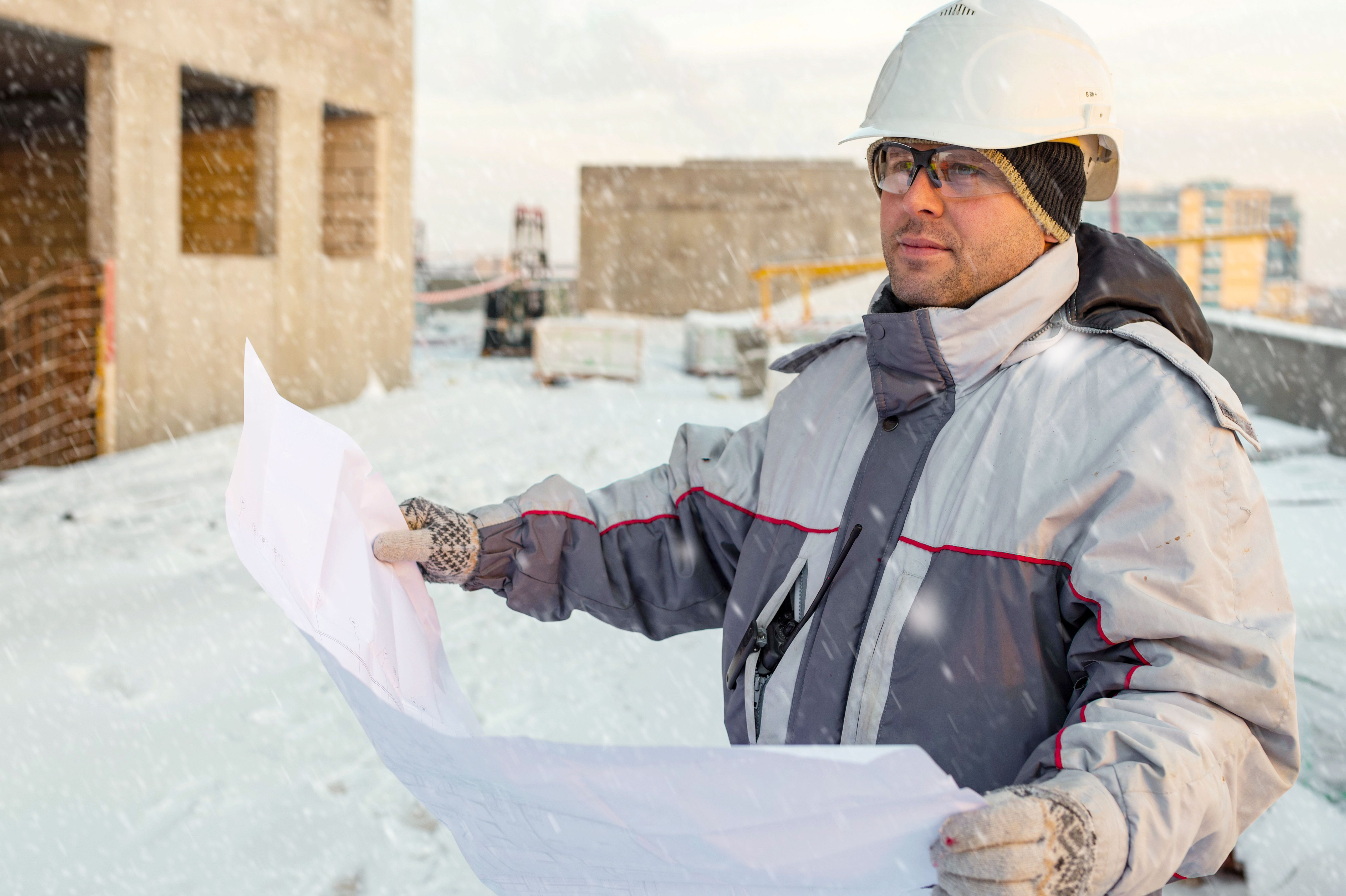 man on a worksite wearing glasses holding plans