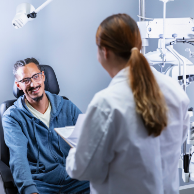 Person receiving an eye exam while a provider reviews notes in a clinical setting